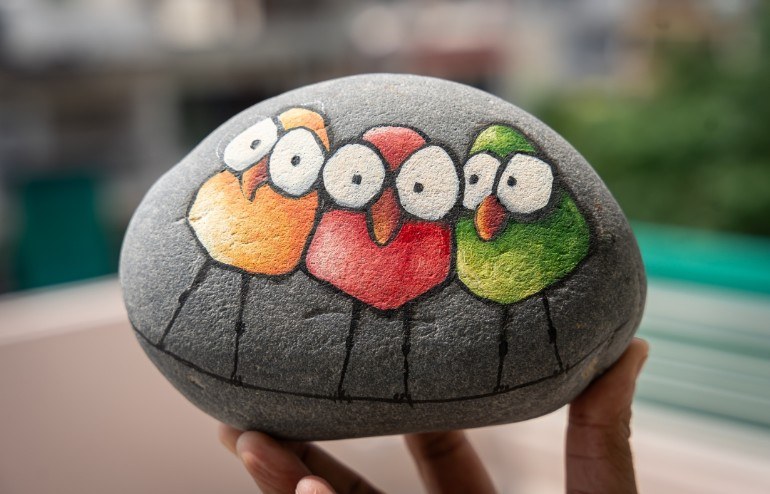 Three cartoon birds on a wire, painted on a grey stone